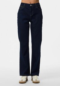 Tumši zili džinsi ar taisnu kāju dizainu, pieci kabatas, metāla pogu aizdare un kontrastējošas šuvju detaļas.