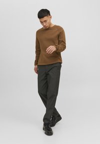 Maglione marrone testurizzato con colletto a girocollo, abbinato a pantaloni grigi scuri a vestibilità ampia e scarpe nere. Design sottile, vestibilità casual.