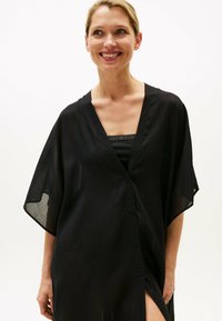 Copricostume nero leggero in stile kimono con scollo a v profondo, maniche corte e chiusura con bottoni, realizzato in tessuto trasparente con dettagli a spacco laterale.