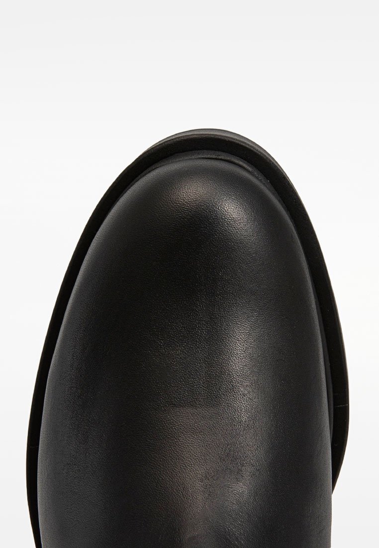 Glatter schwarzer Lederstiefel mit abgerundetem Zehenbereich und sichtbaren Nähten entlang der Kante, fotografiert vor weißem Hintergrund.