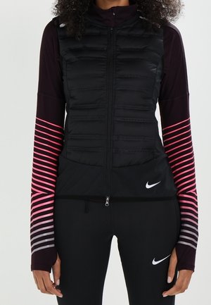 Gilet imbottito nero con chiusura a zip e cuciture orizzontali, abbinato a maniche lunghe con strisce rosa e grigie e aperture per il pollice.