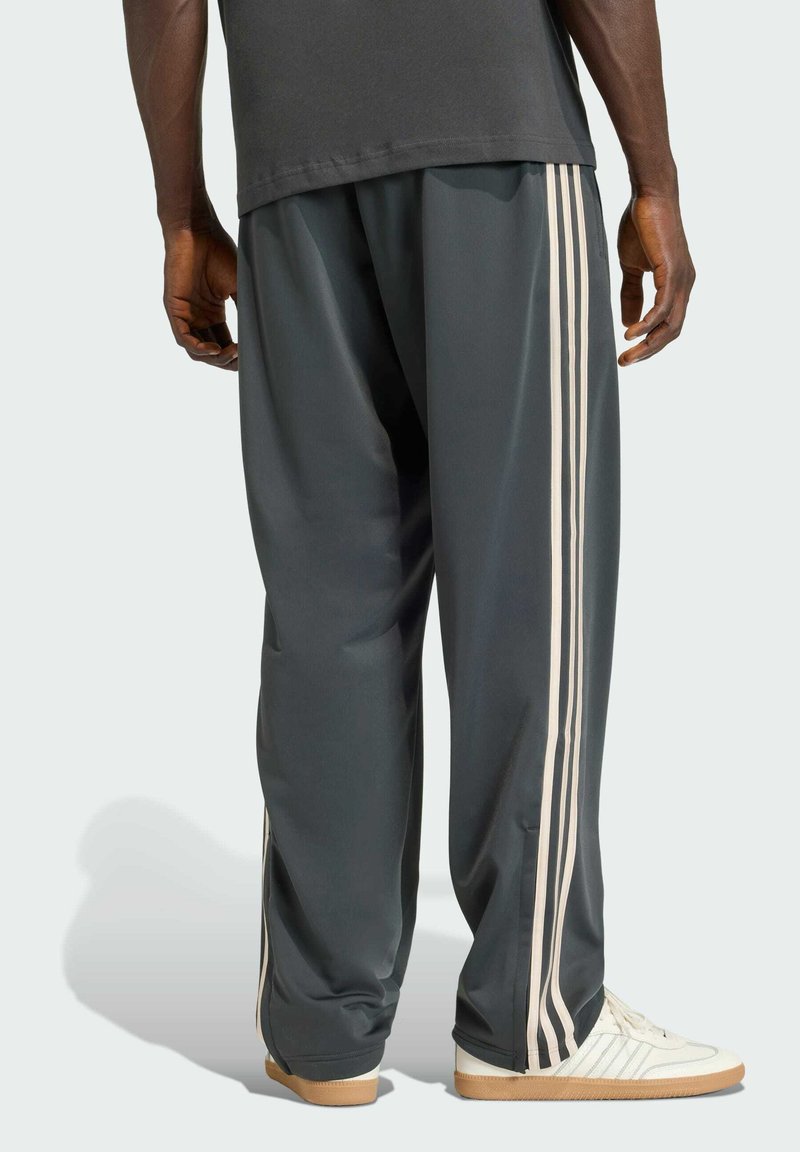 Dunkelgraue Sporthose mit drei weißen vertikalen Streifen an den Seiten, kombiniert mit weißen Sneakern mit strukturierter Sohle.