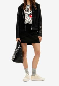 Czarna bluza z kapturem na zamek, graficzny t-shirt z Myszką Miki, czarna spódnica z zakładką, szare skarpetki, beżowe sneakersy oraz teksturowana czarna torebka.