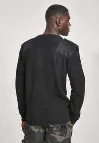 Sudadera negra de punto con textura acanalada, con paneles de cuero en los hombros. Combinada con pantalones cargo de camuflaje.