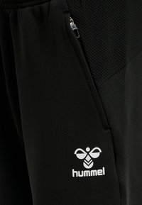 Svarta träningsbyxor med ett nätpanel, ficka med dragkedja och en vit Hummel-logotyp på det nedre benet. Slät yta och åtsittande design.