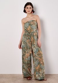 Trägerloser Jumpsuit aus leichtem Stoff mit einem ganzflächigen Palmenblattmuster in erdigen Tönen von Grün, Orange und Blau. Lockere Passform, Taillenbindung.