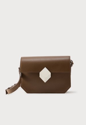 Bruine leren crossbodytas met geometrische witte sluiting en verstelbare riem, geplaatst tegen een eenvoudige lichte achtergrond.