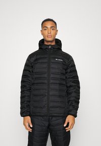Giacca nera isolante con zip frontale, cappuccio e motivo a righe orizzontali. Logo visibile sul lato sinistro del petto.