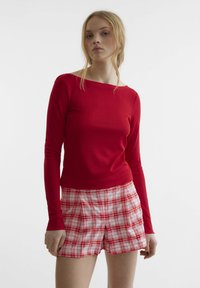 Rotes, geripptes Langarmoberteil kombiniert mit weißen und roten karierten Shorts mit Taschen; beide für einen figurbetonten, lässigen Look entworfen.