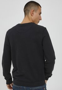 Felpa nera con scollo rotondo, polsini e orlo a costine, realizzata in morbido cotone. Vista dal retro, con una superficie liscia.