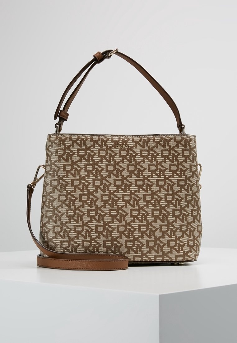 Sac à main marron et beige à motifs avec deux sangles, une bandoulière réglable et une anse plus courte, posé sur une surface blanche.