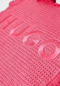 Roze geweven tas met een reliëf "HUGO" logo, een textuurrijk oppervlak en rafelige randen. Het materiaal is zacht met een levendige tint.