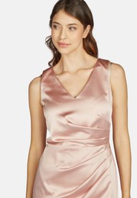 Robe en satin rose clair avec un décolleté en V, sans manches et des détails drapés à la taille. Texture lisse et éclat subtil.