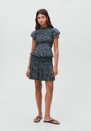 Peplum jurk in blauw en zwart met een gestructureerde stof, voorzien van korte, gerimpelde mouwen en een uitlopende rok. Gedirigeerd met zwarte flip-flops.