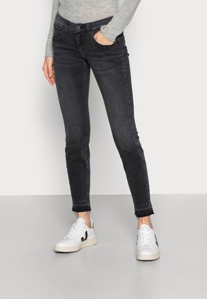 Persona che indossa jeans skinny neri con orli sfrangiati, maglia a maniche lunghe grigia a coste e sneakers bianche con accenti neri.