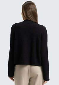 Schwarzer, strukturierter, kurzer Pullover mit langen Ärmeln und rundem Ausschnitt, von hinten vor einem hellgrauen Hintergrund gezeigt.