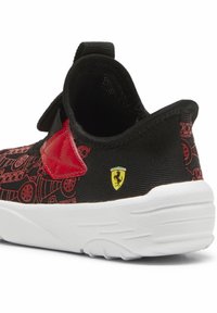 Baskets noires avec des accents rouges, présentant une tige à motif et une semelle blanche. Affiche un logo Ferrari jaune sur le côté.