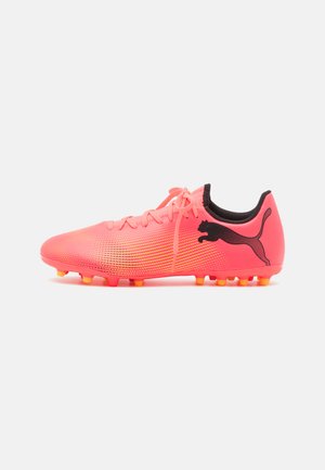 Botas de fútbol rosa brillante con un upper sintético texturizado, acentos negros y tachuelas multicolores para tracción. Presenta el logo en el lateral.