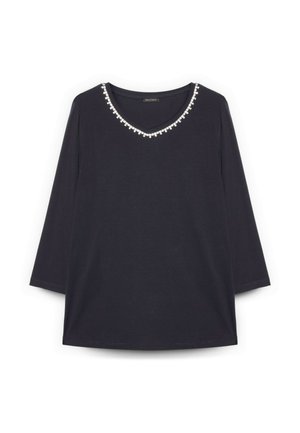 Černý top s dlouhým rukávem a výstřihem do V lemovaným malými bílými dekorativními korálky.