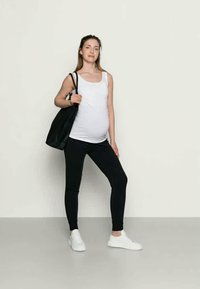 Μαύρο κολάν, λευκό μπλουζάκι και λευκά αθλητικά παπ�ούτσια. Το άτομο κρατάει μια μαύρη τσάντα ώμου, με απαλή υφή υφάσματος και εφαρμοστή σχεδίαση.