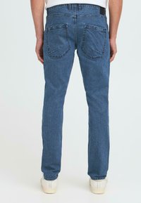 Blauwe spijkerbroek met een straight leg ontwerp, twee achterzakken met schuine naden en een klassieke tailleband, gecombineerd met witte sneakers.