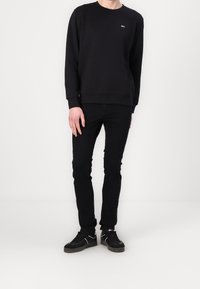 Svart sweatshirt med rund hals och ribbade ärmar, kombinerad med svarta slim-fit jeans och svarta sneakers med vita detaljer. Enkelt design.