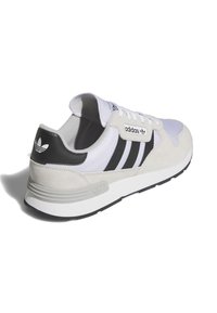 Tenisi albi și negri cu un exterior din suede și plasă, trei dungi negre, șireturi albe și un guler căptușit. Talpa gri cu detalii texturate.