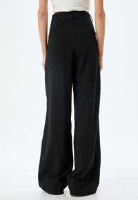 Pantalons larges taille haute noirs avec une texture lisse, dotés de poches arrière et d'un design épuré et minimaliste.