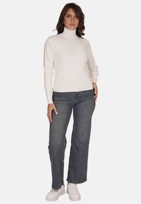 Maglione bianco a collo alto realizzato in tessuto morbido, abbinato a jeans azzurri a vita alta e sneakers bianche; design semplice e aderente senza motivi.