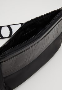 Borsa a tracolla nera con una striscia in pelle testurizzata e a fantasia. Presenta una chiusura con zip e una tracolla a fantasia. Interno in tessuto liscio.