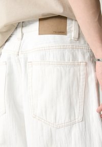 Jean en denim blanc avec une finition texturée, dotée de poches arrière et d'une étiquette en cuir beige estampillée "PULL&BEAR" sur la ceinture.