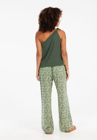 Top verde de un solo hombro combinado con pantalones de pierna ancha con un diseño geométrico en verde, amarillo y blanco; ajuste relajado y tela suave.