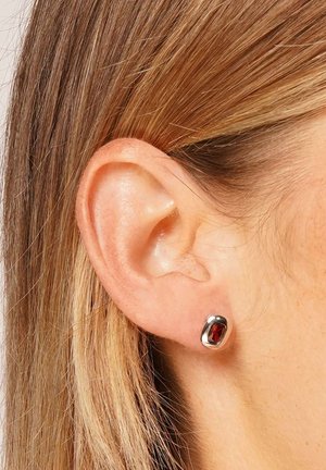 Silver stud earrings featuring a rounded design with a deep red gemstone in the center, set against a neutral background.