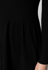 Svart stickad klänning med ribbad överdel och flytande kjol. Tyget är mjukt med en slät yta, lämpligt för vardagsbruk.