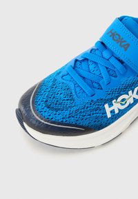 Baskets de course bleu avec une tige en maille texturée, logo blanc, bout arrondi et semelle blanche. Comprend un système de fermeture à lacets et à sangle.