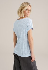 Gaiši zils īsām piedurknēm tops ar teksturētu herringbone rakstu, apaļu kakla izgriezumu un sarullētām piedurknēm. Saskaņots ar tumšiem brīvi pieguļošiem biksēm.