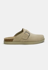 Beige klompen met een bovenkant van suede, verstelbare band en kurken voetbed. Rubberen zool met kleine profiel voor grip. Eenvoudig, open achterkant ontwerp.