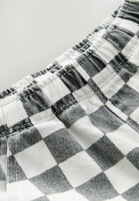 Tissu à carreaux noir et blanc, avec un waistband élastique froncé et un détail de couture visible, présenté en gros plan.