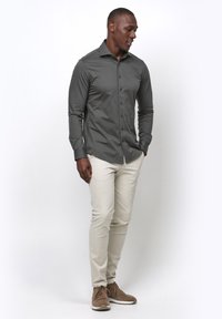 Donkergrijze lange mouwen overhemd met knopen in een slim fit, gecombineerd met lichtbeige slim-fit broek en bruine veterschoenen.