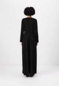 Langes schwarzes Kleid mit tailliertem Oberteil, langen Ärmeln und ausgestellt geschnittenem Saum. Verfügt über einen Reißverschluss im Rücken und dezente Falten für eine glatte Textur.