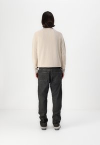 Suéter de punto beige con cuello redondo, combinado con jeans grises de corte holgado y zapatos grises, visto desde la parte trasera.