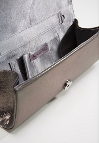 Grå metallisk clutchväska med slät yta, tryckknappsstängning och innerficka med etikett. Kompakt och stilren design.