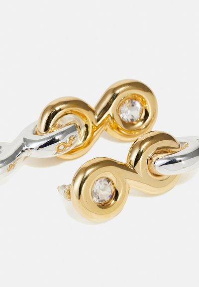 Gold- und Silberohrringe mit einem verdrehten Design, zwei klaren Edelsteinen und einer polierten Oberfläche. Die Formen erzeugen einen ineinandergreifenden Look.