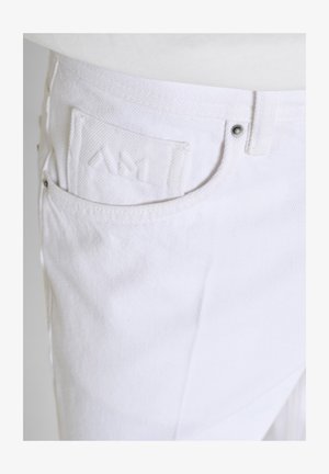 Bijele traper hlače u krupnom planu prikazuju prednji džep s diskretnim vezenim logotipom i metalnim nitnama.