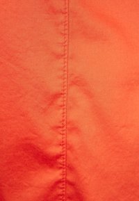 Tessuto arancione brillante con una superficie liscia e una leggera lucentezza, caratterizzato da una cucitura verticale prominente che corre lungo il centro.