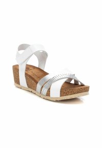 Sandalias de cuña blancas con detalles plateados entrelazados, plantilla de corcho y suela texturizada. Las correas ofrecen un ajuste seguro.