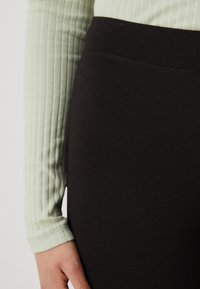 Svarta stretchbyxor med en slät textur och hög midja, ihop med en ljusgrön ribbad långärmad topp.