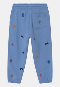 Pantalones de chándal azules con varios diseños bordados coloridos: árboles, montañas y personajes; detalle de cintura elástica y bolsillo trasero.