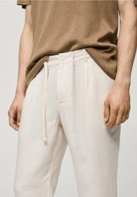 Světlé béžové lněné kalhoty s vertikálními pruhy, s elastickým pasem na šňůrku, knoflíkovým zapínáním a kapsami. Texturovaná látka zvyšuje vizuální zajímavost.