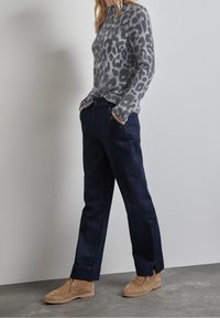 Maglione grigio con stampa leopardata, jeans dritti blu scuro e stivali in camoscio beige, con tasche laterali e dettagli con bottoni sui jeans.